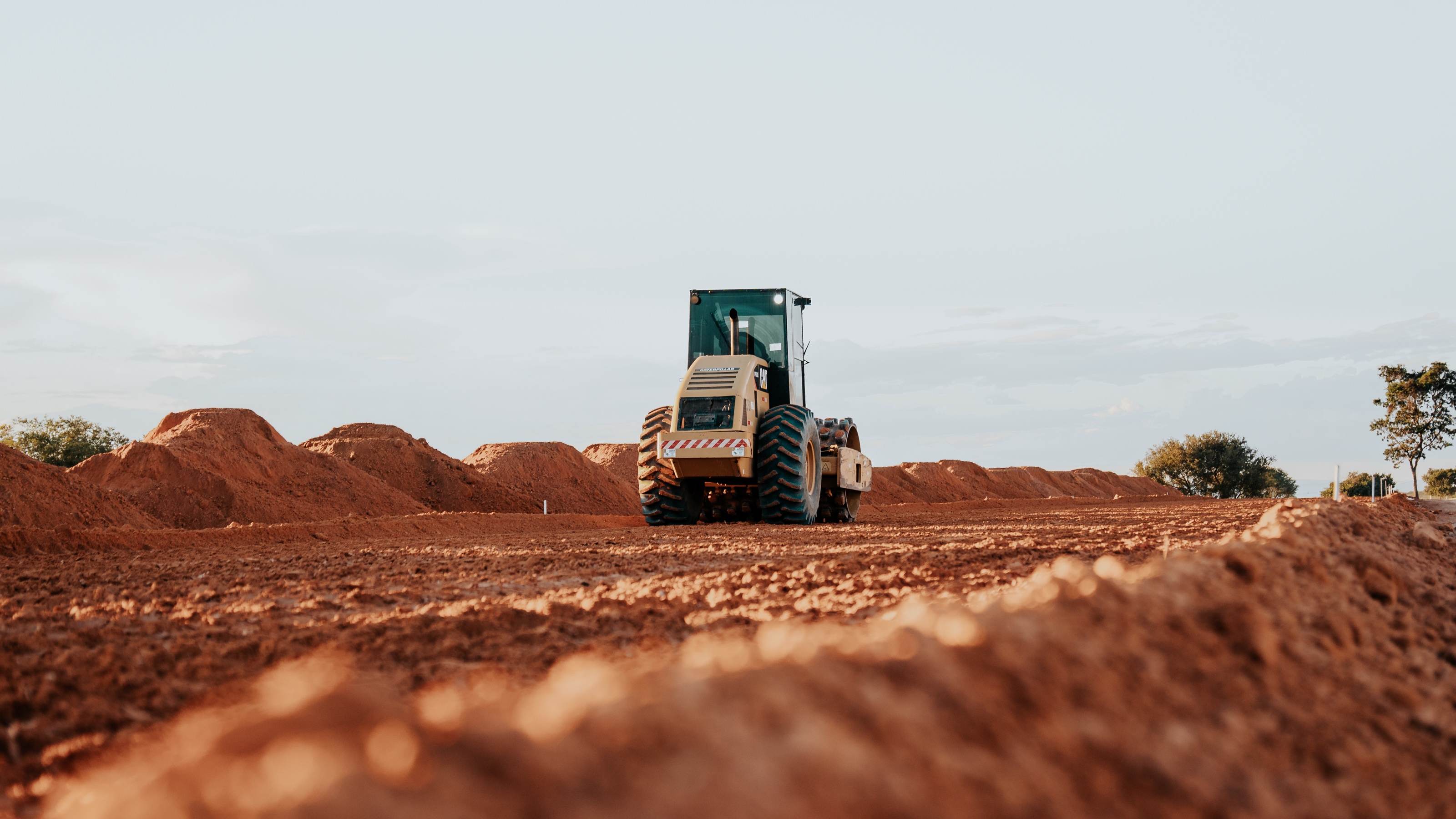 Rolo compactador trabalhando na terra vermelha ao fim da tarde