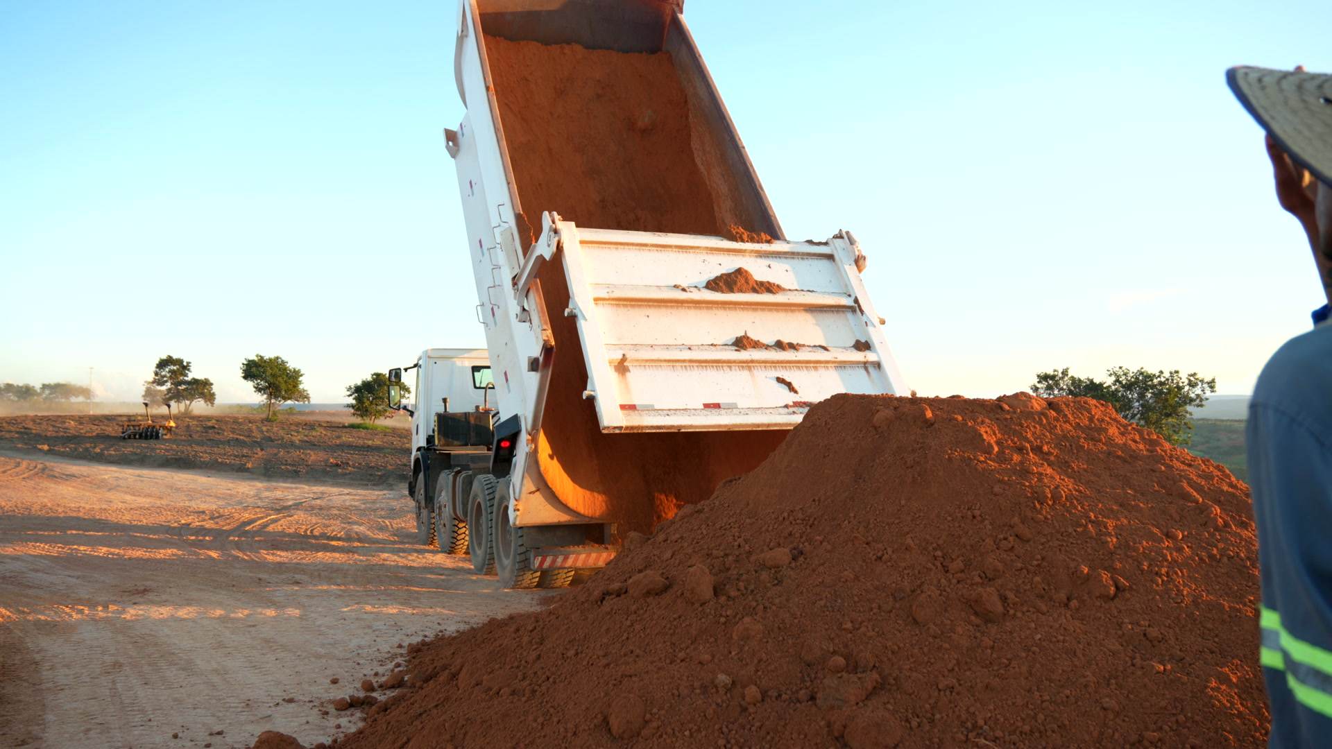 Caminhão basculando material, com técnico em campo