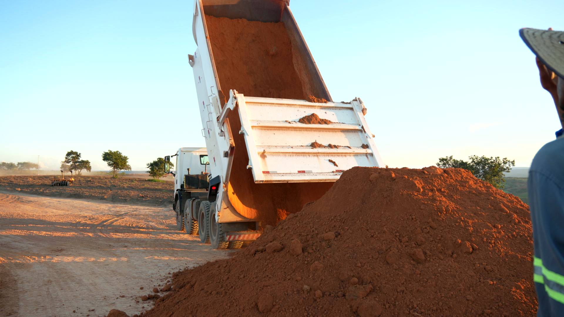Caminhão basculando material, com técnico em campo